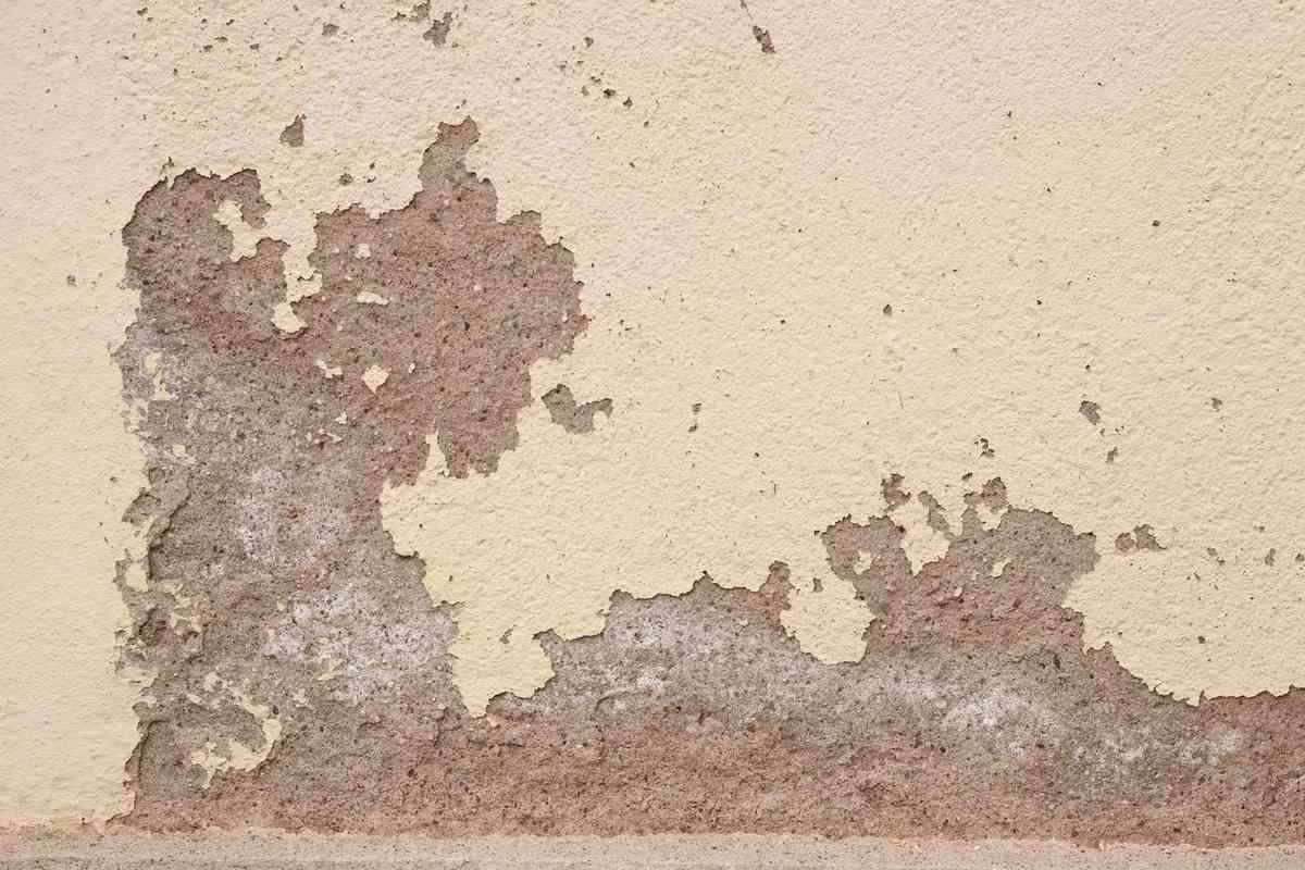 Enduit qui s'écaille sur un mur beige révélant la couche grise