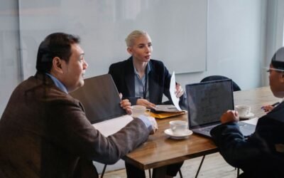 Trois personnes discutent autour d'une table avec ordinateurs et documents